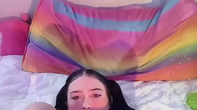 Brunette with pigtails, lipstick and a dildo among rainbow pillows